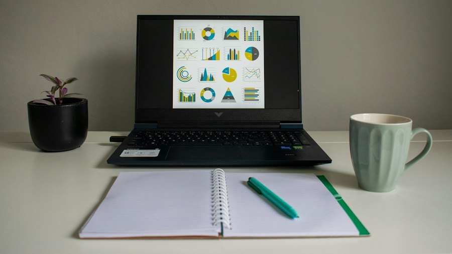 Laptop displaying a collection of charts beside a notebook